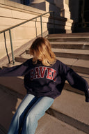 Person wearing a navy blue mockneck with a 'SAVED' appliquee on the front, sitting on steps outdoors.
