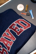 Navy blue mockneck sweatshirt with 'SAVED' applique, makeup items on a pilates reformer.